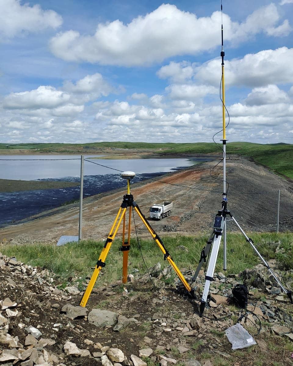 GNSS engineering survey equipment on tripods on a dam embankment beside a reservoir