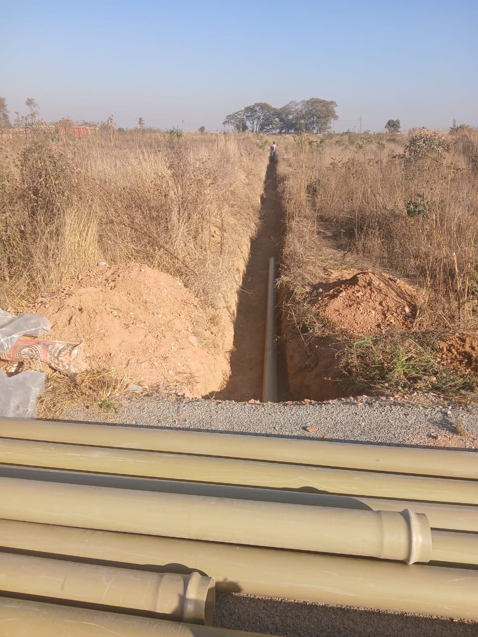 Sewer pipe laid along a long narrow trench with stacked pipes in the foreground