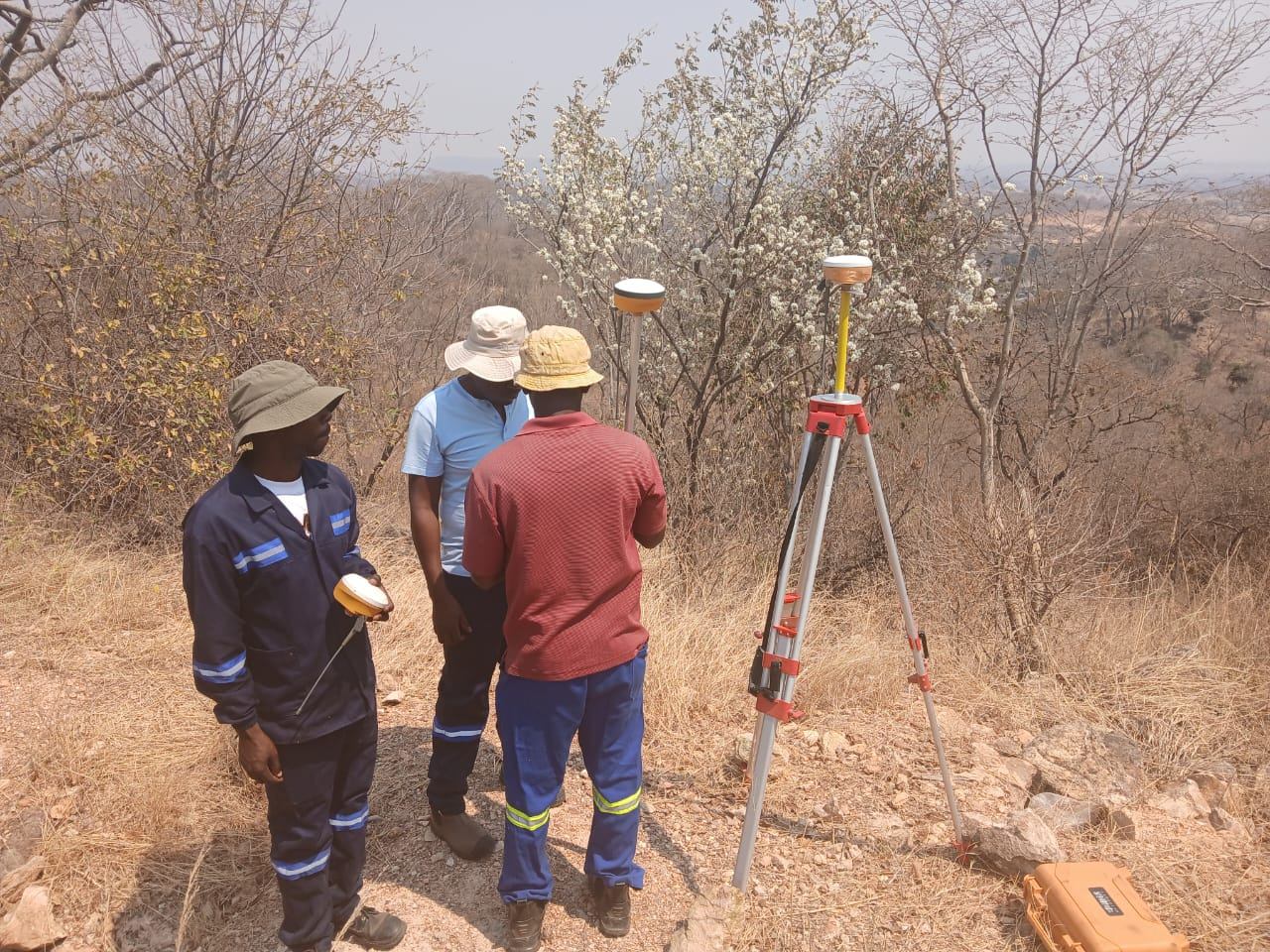 Survey team setting up GNSS receivers on a tripod and pole for a topographical survey on a hillside in Kadoma